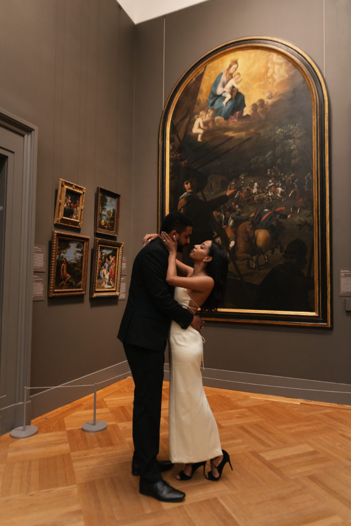 man and woman hugging and looking at each other while in front of art at the met