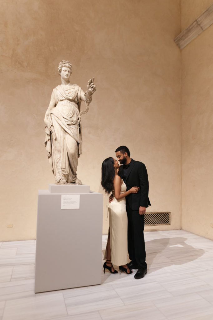 woman and man posing and hugging in front of statue at the met